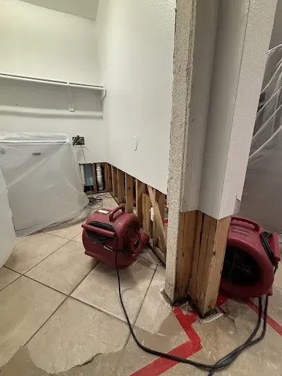 Baseboards removed and air movers drying the base of a wall in a Sugar Land home